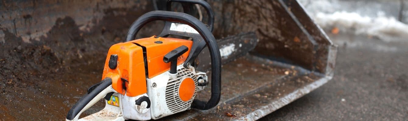 A chainsaw sits on a piece of heavy lawn equipment.